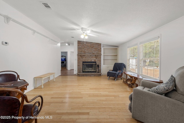 living room with vaulted ceiling, a stone fireplace, built in features, a textured ceiling, and light wood-type flooring