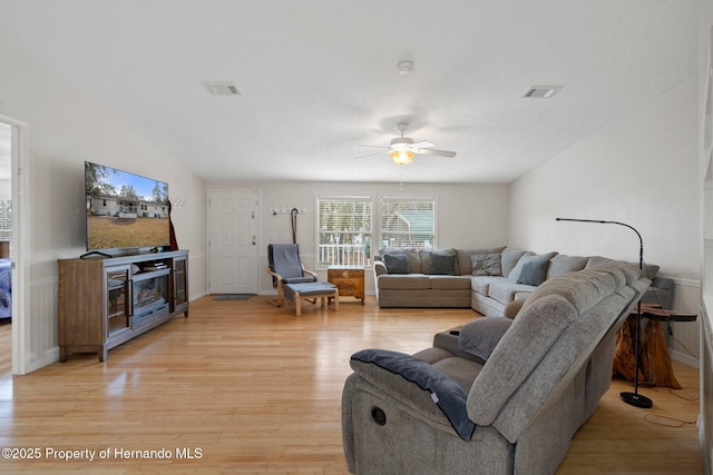 living room with ceiling fan, a textured ceiling, and light wood-type flooring