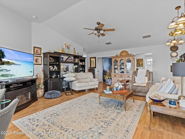 living room with lofted ceiling, ceiling fan with notable chandelier, and light hardwood / wood-style flooring