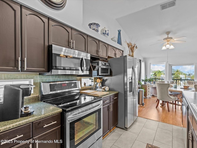 kitchen with appliances with stainless steel finishes, tasteful backsplash, lofted ceiling, light tile patterned floors, and dark brown cabinetry