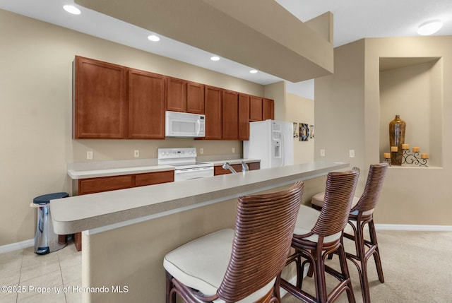 kitchen featuring a breakfast bar area, recessed lighting, light countertops, white appliances, and baseboards