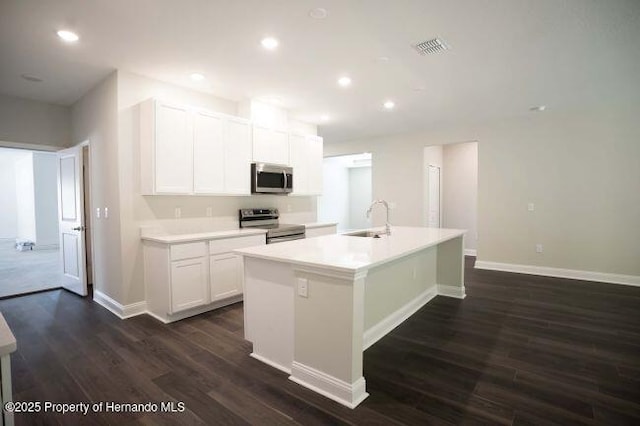 kitchen with appliances with stainless steel finishes, white cabinetry, sink, dark hardwood / wood-style flooring, and a center island with sink