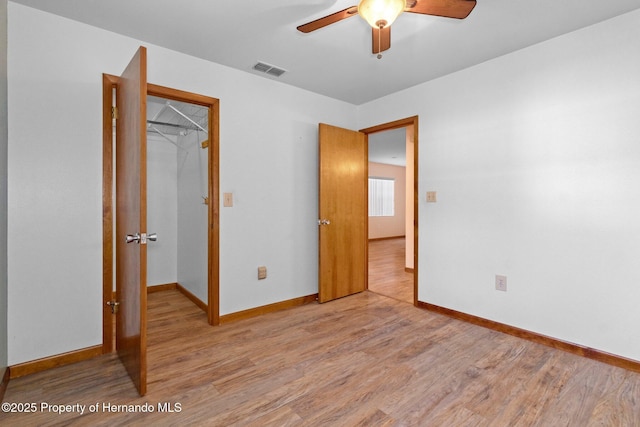 unfurnished bedroom with a closet, a walk in closet, ceiling fan, and light hardwood / wood-style flooring