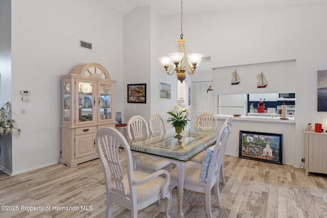 dining space featuring high vaulted ceiling, an inviting chandelier, and light wood-type flooring