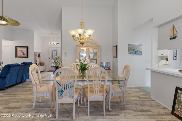 dining area with an inviting chandelier, washer / dryer, light wood-type flooring, and a high ceiling