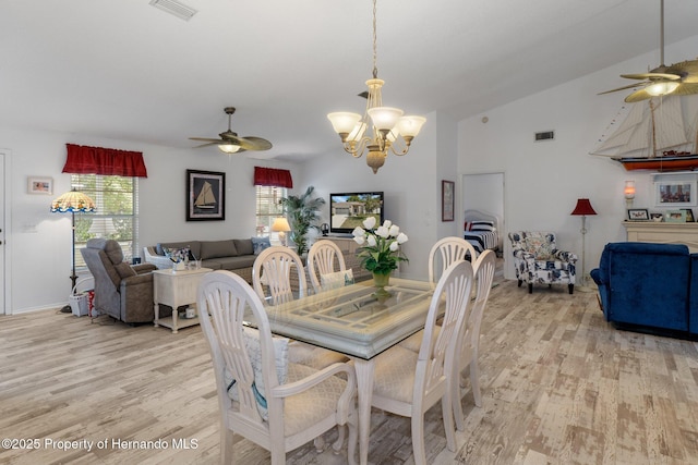 dining room with ceiling fan with notable chandelier, a wealth of natural light, lofted ceiling, and light hardwood / wood-style flooring