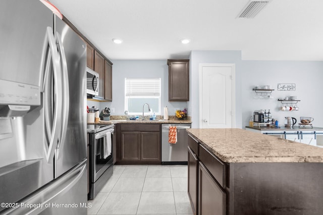 kitchen featuring light tile patterned flooring, appliances with stainless steel finishes, sink, a center island, and dark brown cabinets