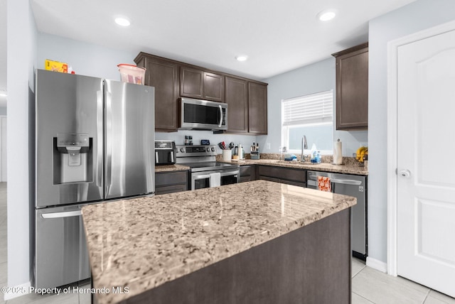 kitchen with stainless steel appliances, a kitchen island, light stone countertops, and sink