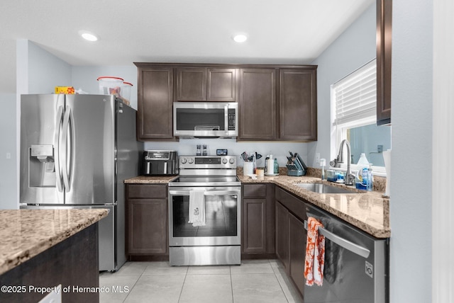 kitchen with appliances with stainless steel finishes, sink, light tile patterned floors, and light stone counters