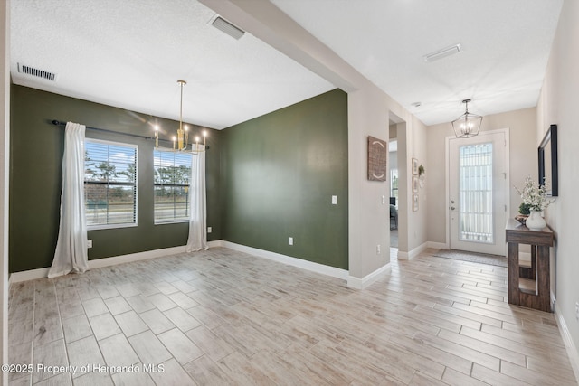 foyer entrance featuring a textured ceiling, an inviting chandelier, and light hardwood / wood-style floors