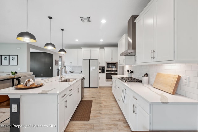 kitchen with appliances with stainless steel finishes, sink, hanging light fixtures, wall chimney exhaust hood, and a spacious island