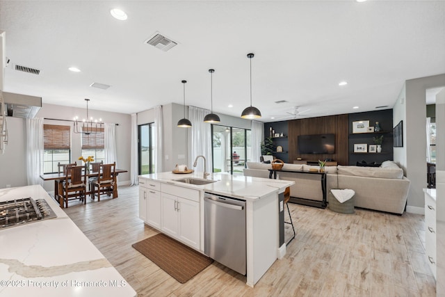 kitchen with appliances with stainless steel finishes, pendant lighting, white cabinetry, sink, and a kitchen island with sink