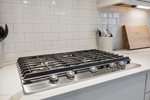 interior details with light stone countertops, stainless steel gas cooktop, and backsplash