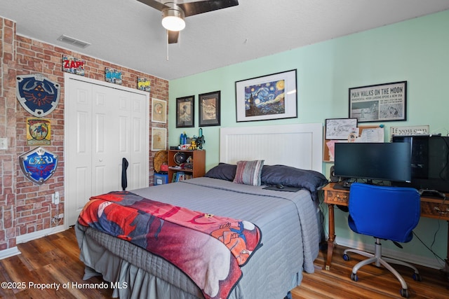 bedroom with ceiling fan, wood-type flooring, a textured ceiling, brick wall, and a closet