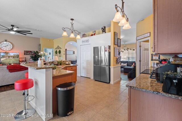 kitchen with light tile patterned floors, stainless steel refrigerator, hanging light fixtures, a kitchen breakfast bar, and light stone countertops