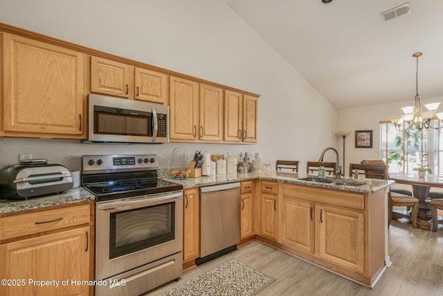 kitchen with appliances with stainless steel finishes, sink, hanging light fixtures, kitchen peninsula, and light stone countertops