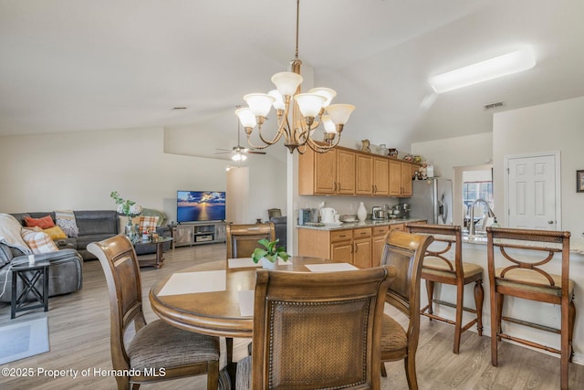 dining space featuring sink, light hardwood / wood-style floors, vaulted ceiling, and a notable chandelier