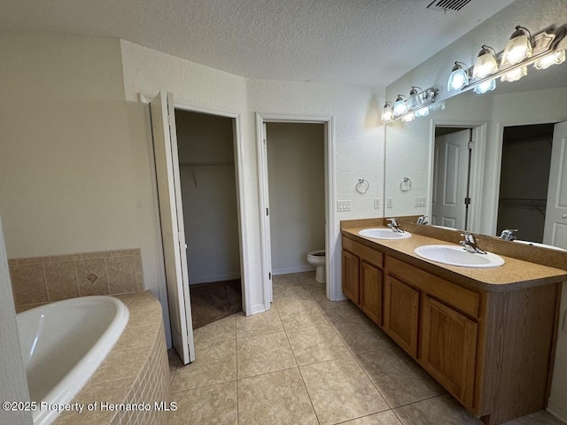 bathroom featuring tile patterned floors, toilet, a textured ceiling, vanity, and tiled tub