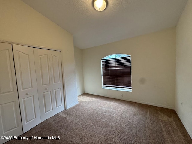 unfurnished bedroom featuring lofted ceiling, carpet floors, a closet, and a textured ceiling