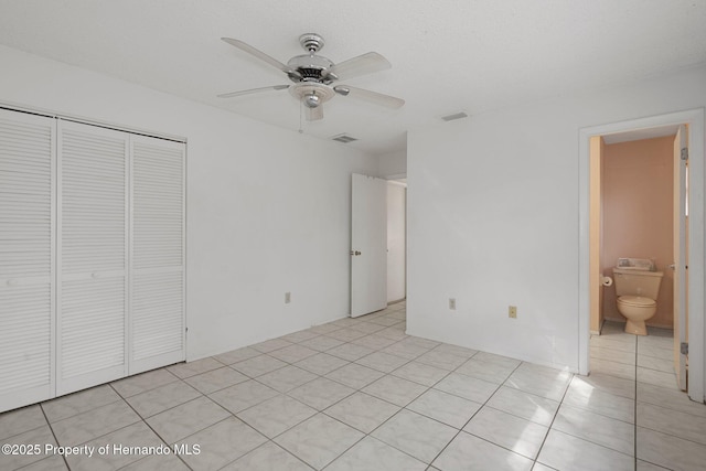 unfurnished bedroom featuring ceiling fan, connected bathroom, a closet, and light tile patterned floors