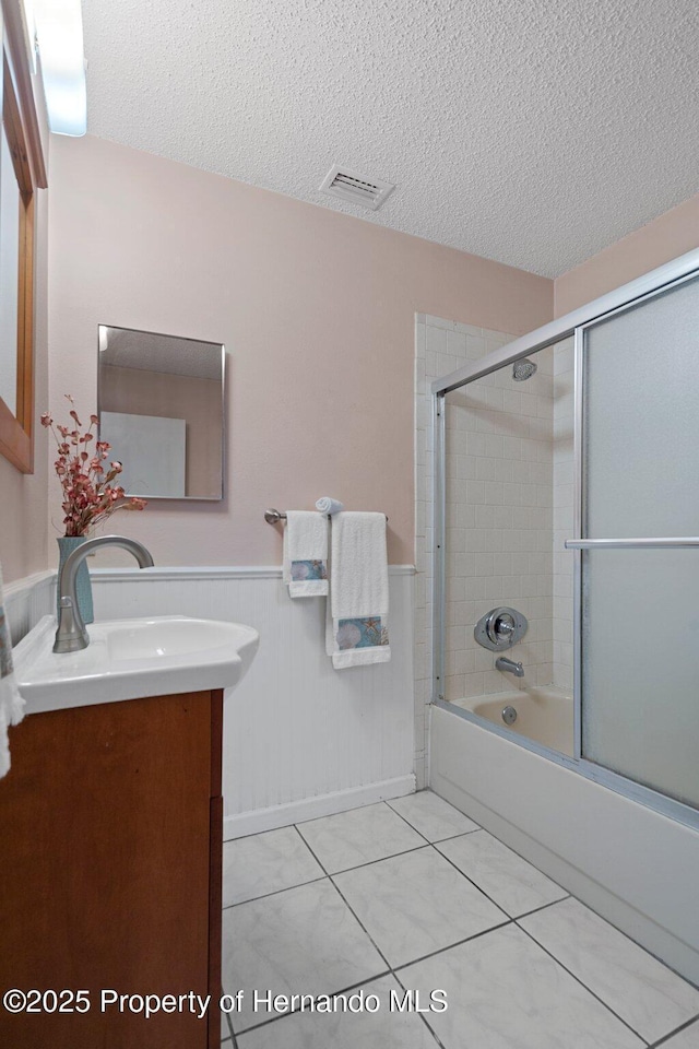 bathroom featuring tile patterned flooring, enclosed tub / shower combo, vanity, and a textured ceiling