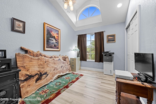 interior space featuring light wood-style flooring, vaulted ceiling, a textured wall, baseboards, and a ceiling fan