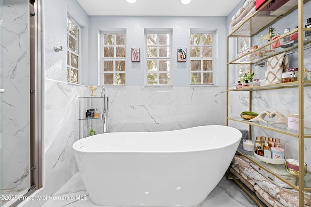 bathroom with a freestanding tub, marble finish floor, and tile walls