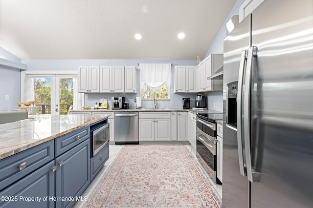 kitchen with white cabinetry, light stone counters, appliances with stainless steel finishes, and vaulted ceiling