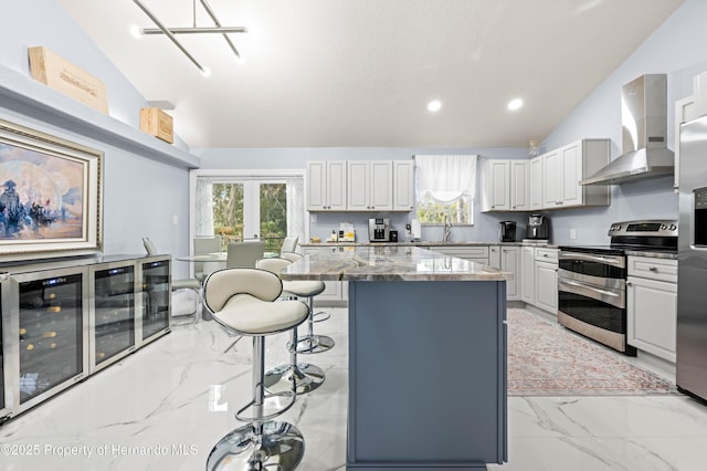 kitchen with appliances with stainless steel finishes, marble finish floor, vaulted ceiling, a kitchen bar, and wall chimney exhaust hood