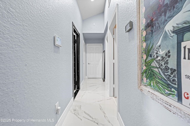 hallway featuring baseboards, a textured wall, and marble finish floor