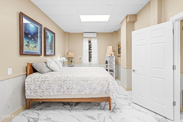 bedroom featuring a drop ceiling, marble finish floor, and wainscoting