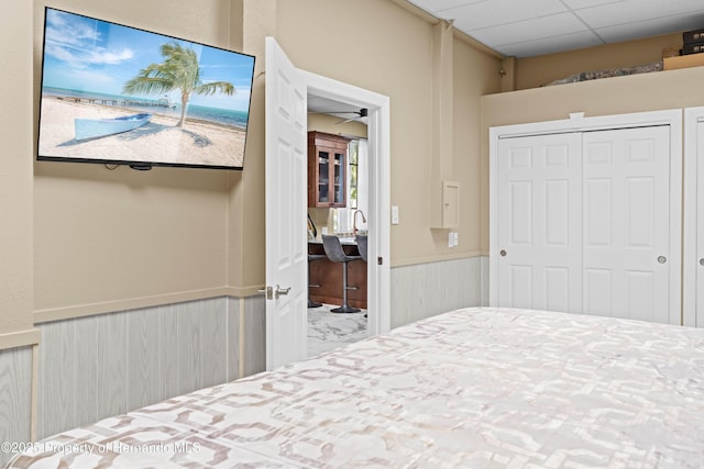 bedroom with a drop ceiling, a closet, and wainscoting