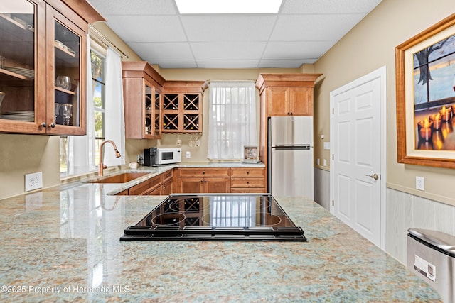 kitchen with light stone countertops, white microwave, freestanding refrigerator, a sink, and stovetop