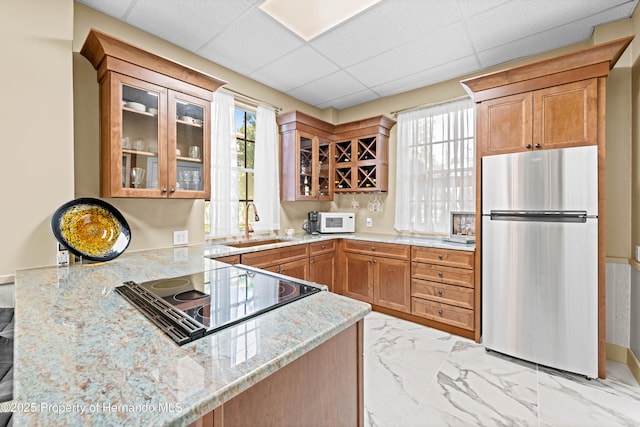 kitchen with light stone countertops, glass insert cabinets, stovetop with downdraft, white microwave, and freestanding refrigerator