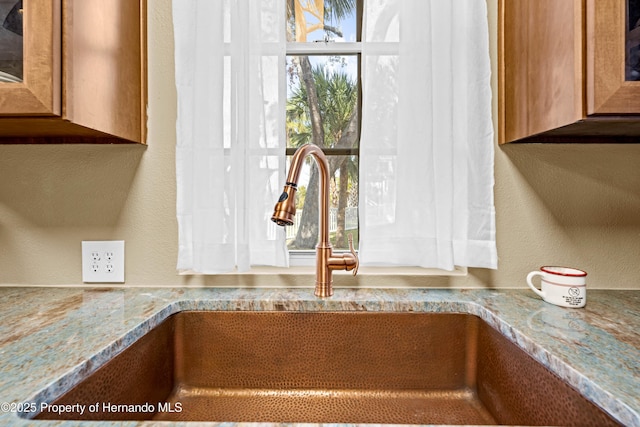 interior details featuring light stone countertops, brown cabinetry, a textured wall, and a sink