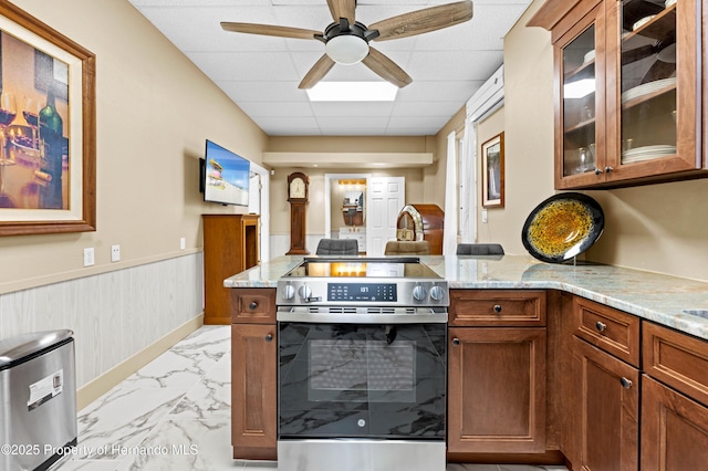 kitchen with light stone counters, electric stove, a peninsula, marble finish floor, and wainscoting