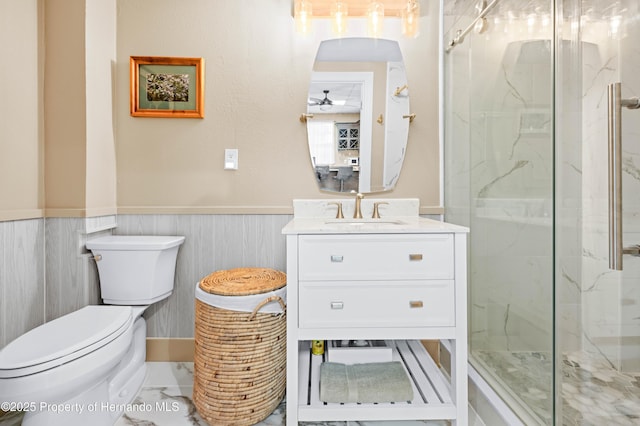 full bathroom featuring ceiling fan, a wainscoted wall, a marble finish shower, toilet, and vanity