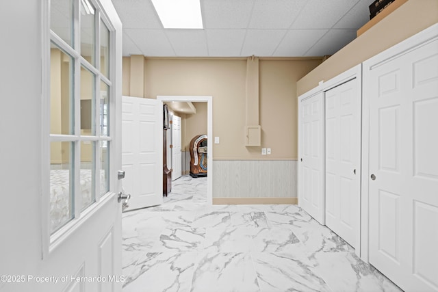 hallway with a wainscoted wall, marble finish floor, and a paneled ceiling