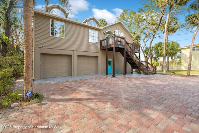 view of front of house featuring stairway, stucco siding, decorative driveway, a deck, and an attached garage