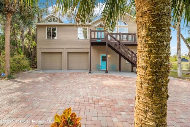 beach home featuring stucco siding, decorative driveway, stairs, and an attached garage