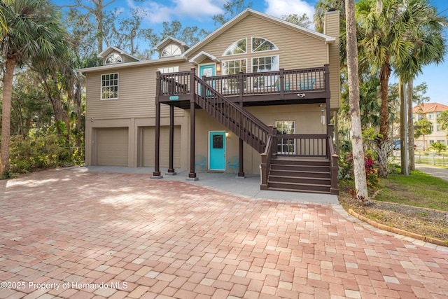 rustic home with stairs, a deck, a chimney, decorative driveway, and a garage
