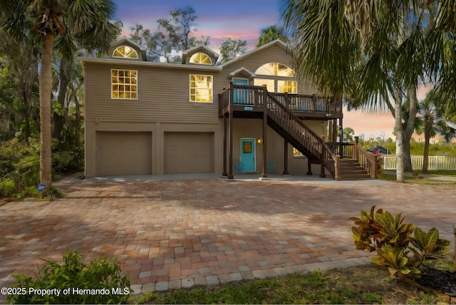 coastal inspired home with decorative driveway, stairs, a garage, and a wooden deck