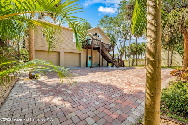 beach home with a wooden deck, a garage, stairway, decorative driveway, and stucco siding