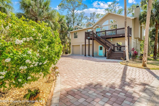 view of front of house featuring a deck, a chimney, decorative driveway, stairs, and an attached garage