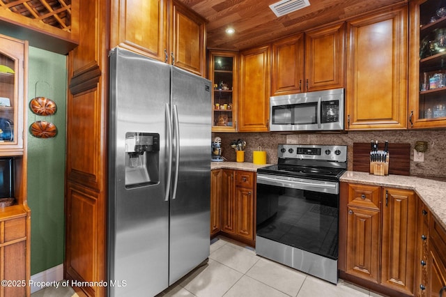 kitchen with light stone countertops, appliances with stainless steel finishes, light tile patterned floors, and backsplash