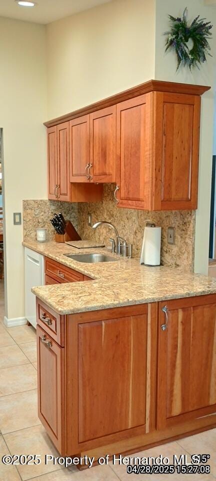 kitchen with light stone counters, light tile patterned floors, tasteful backsplash, a sink, and white dishwasher