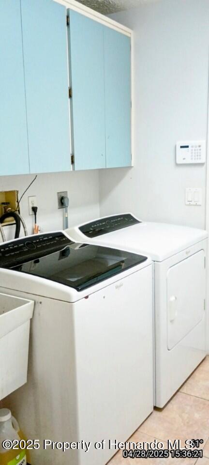 clothes washing area featuring cabinet space, light tile patterned flooring, and washing machine and dryer