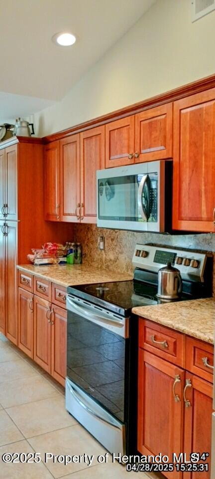 kitchen with brown cabinets, decorative backsplash, visible vents, stainless steel appliances, and light tile patterned flooring