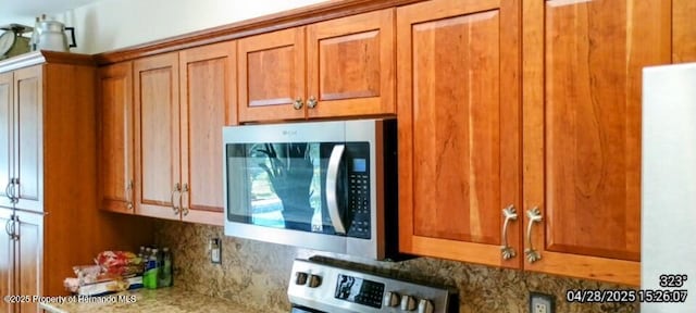details with stainless steel microwave, range, light countertops, brown cabinets, and backsplash