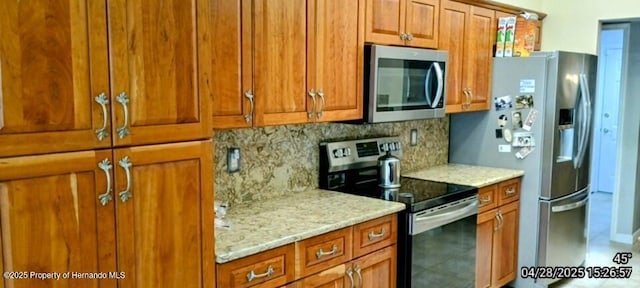 kitchen with light stone countertops, backsplash, appliances with stainless steel finishes, and brown cabinets